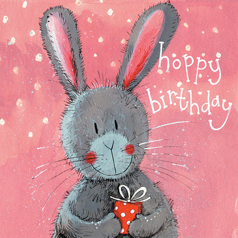 Grey bunny rabbit holding a present on a pink background with Hoppy birthday written on front