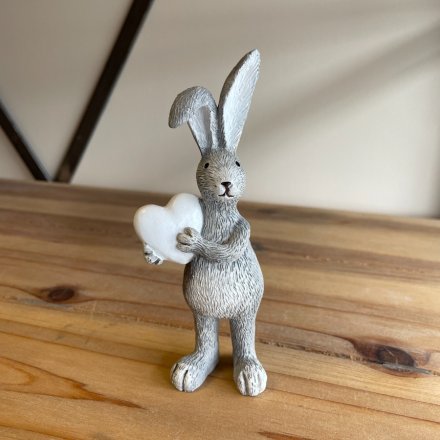 Standing rabbit figure in grey with upright ears who is holding a white heart